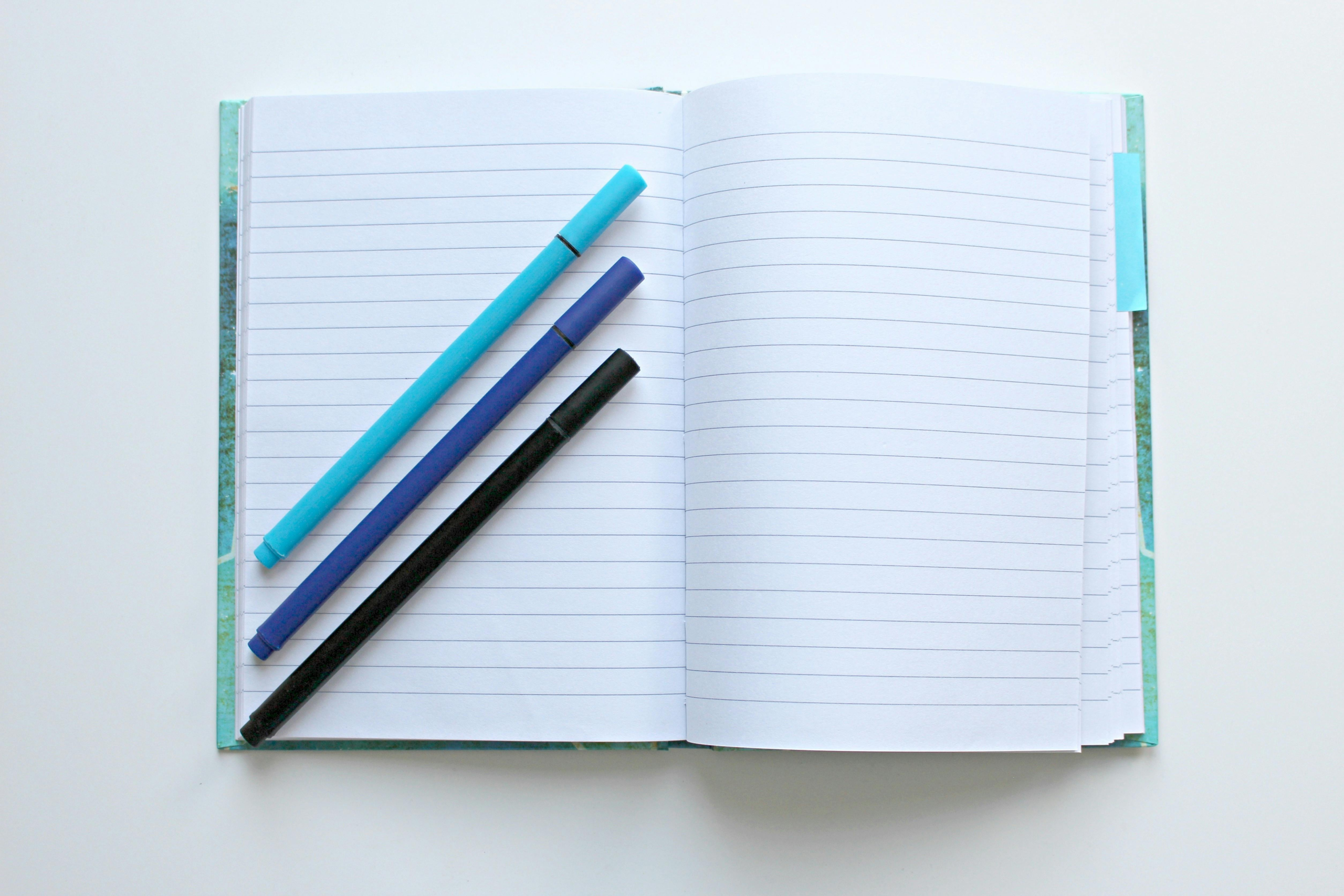 Open lined notebook with three pens resting across the pages